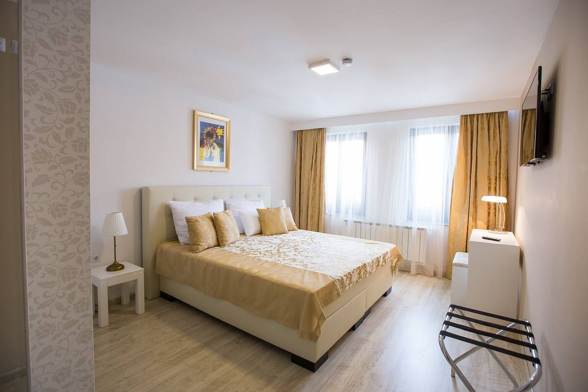 Une chambre d’hôtel avec un grand lit, une table de chevet avec une lampe, un téléviseur fixé au mur et une fenêtre avec des rideaux.