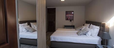 Ein Hotelzimmer mit zwei Betten, Holzboden, Spiegel, Tür, Nachttisch mit Lampe und einem an der Wand montierten Fernseher.