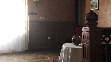 A room with a wooden floor, a dining table with chairs, a chandelier, and a large window with sheer curtains.
