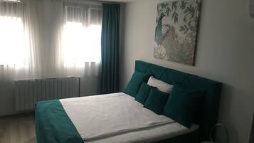 A bedroom with a bed, a radiator, a window with curtains, and a wall-mounted artwork.