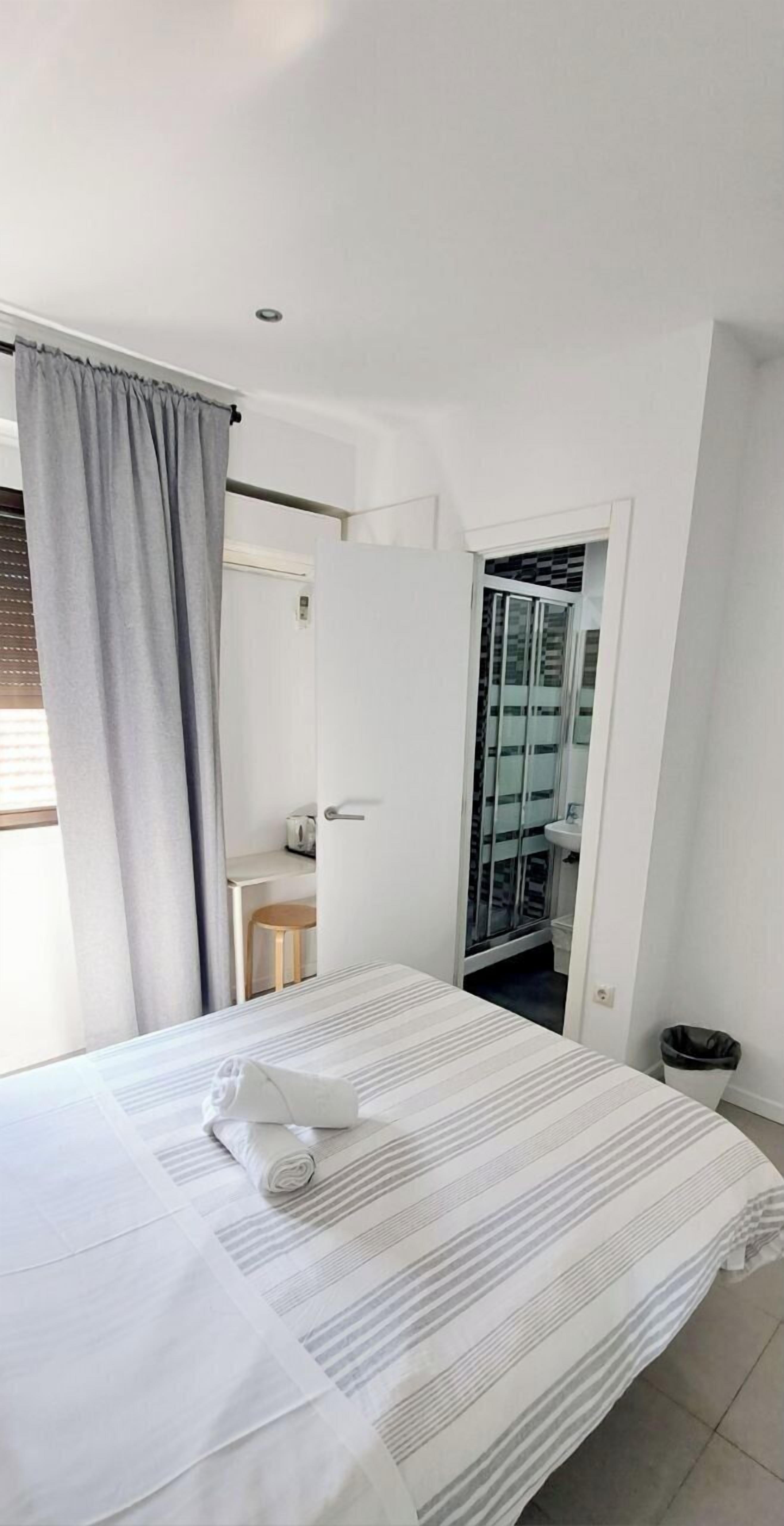 A hotel room with a bed, a bathroom visible through an open door, and a window with curtains.