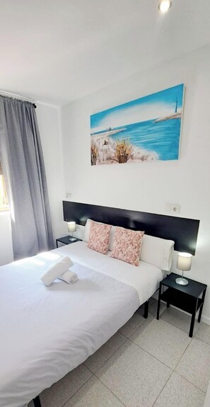 A neatly made bed with a white comforter and two pink floral pillows, a black headboard, and a painting of a coastal scene above the bed. - AYZ Sierra de Meira - Auto check-in property (Madrid)