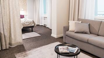 A hotel room with a bed, a sofa, a coffee table with a magazine, and a window with curtains.