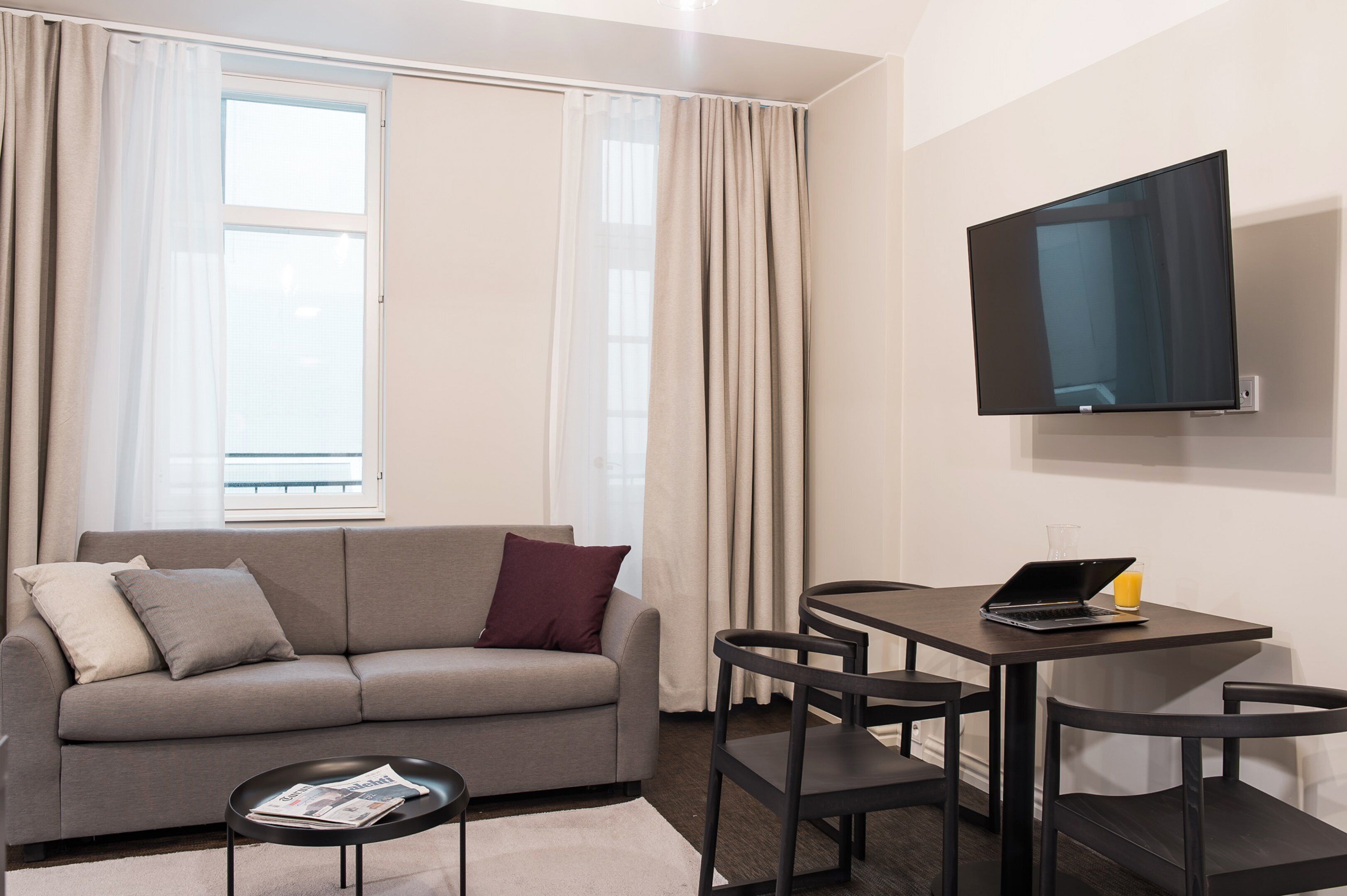 A modern living room with a sofa, a coffee table, a TV mounted on the wall, and a small dining table with chairs.