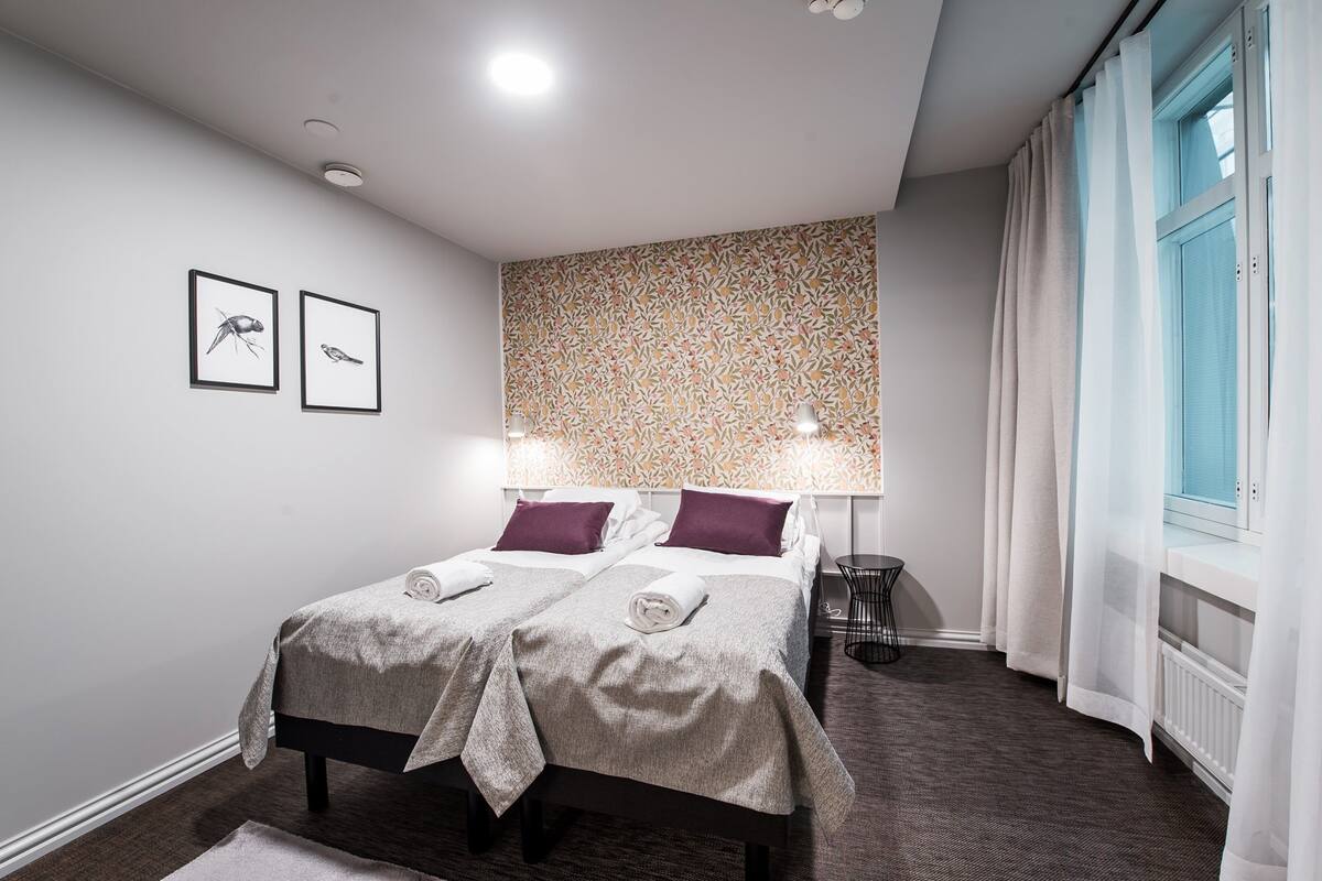 A neatly arranged bedroom with a bed, two pillows, a bedside table, a lamp, and two framed pictures on the wall.