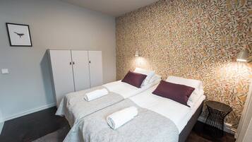 Habitación de hotel con dos camas, un armario, una mesita pequeña y una pared con estampado floral.