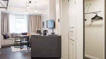 A modern, well-lit room with a dining area, kitchenette, and a seating area with a sofa and cushions.