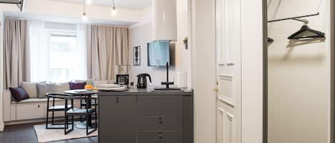 A modern, well-lit room with a dining area, kitchenette, and a seating area with a sofa and cushions.
