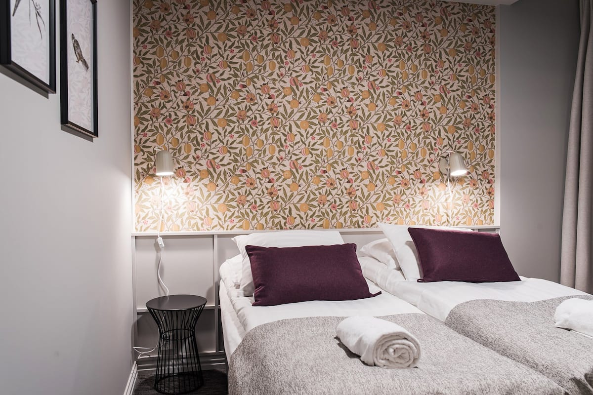 A hotel room with two beds, a small table, and a wall with a floral pattern.