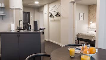A hotel room with a kitchenette, a dining area with a table set for two, and a bed with a headboard.