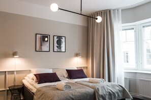 A hotel room with a bed, two bedside lamps, a window with curtains, and two framed pictures on the wall. - Forenom Aparthotel Turku (Turku)