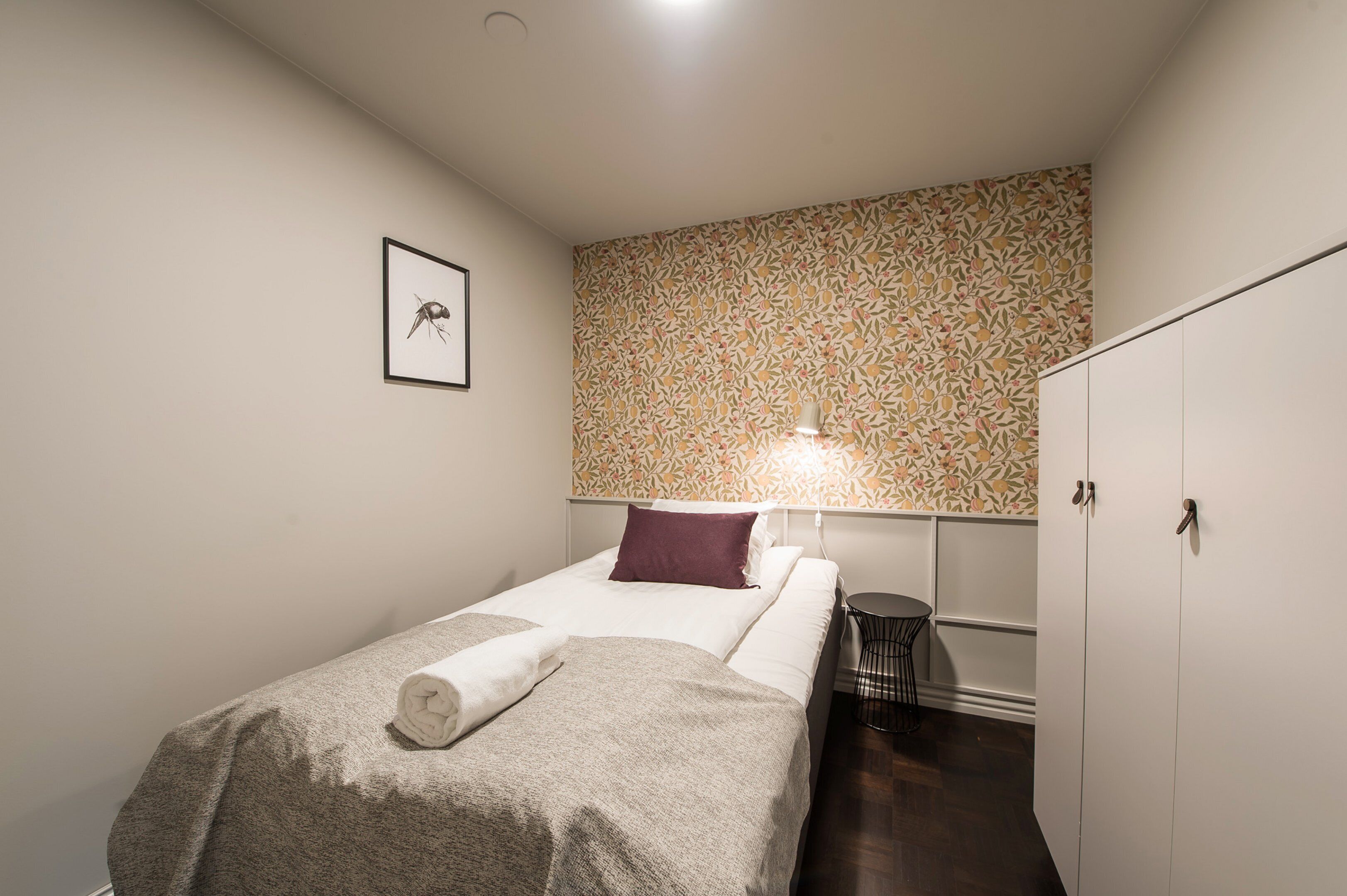 A small, neatly arranged bedroom with a bed, a bedside table, a lamp, and a wardrobe.