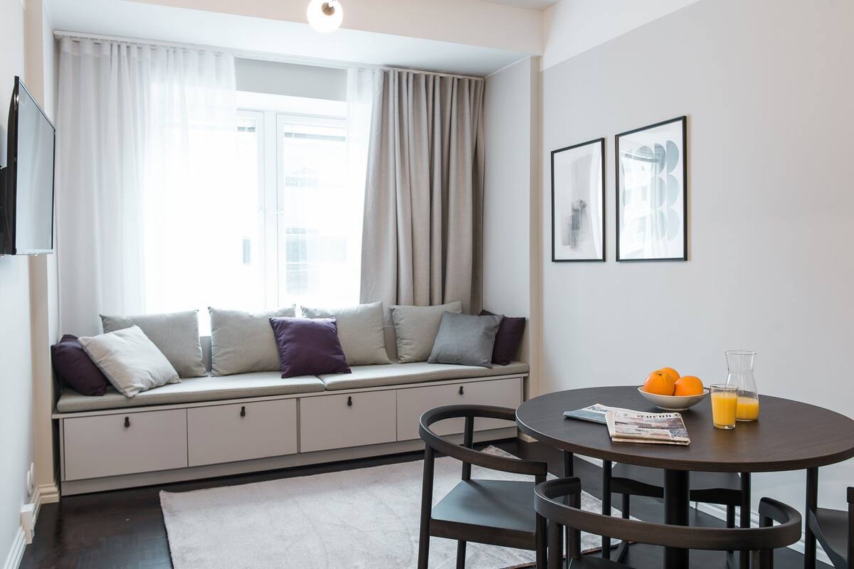 A modern living room with a built-in bench, a round dining table, and a window with curtains.