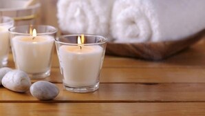 Tres velas encendidas en recipientes de vidrio transparente sobre una superficie de madera, con una toalla blanca enrollada al fondo.