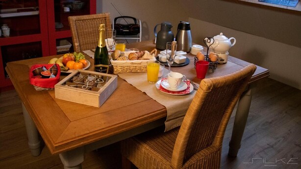 Mesa de desayuno dispuesta con frutas, pan, una botella de champán, café y té.