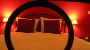 Una cama con almohadas rojas y dos lámparas de noche en una habitación con paredes rojas.