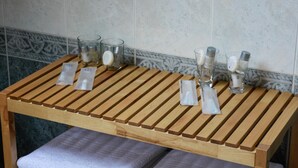Una mesa de madera con cuatro recipientes de vidrio y sobres, probablemente para artículos de aseo, frente a una pared de azulejos.