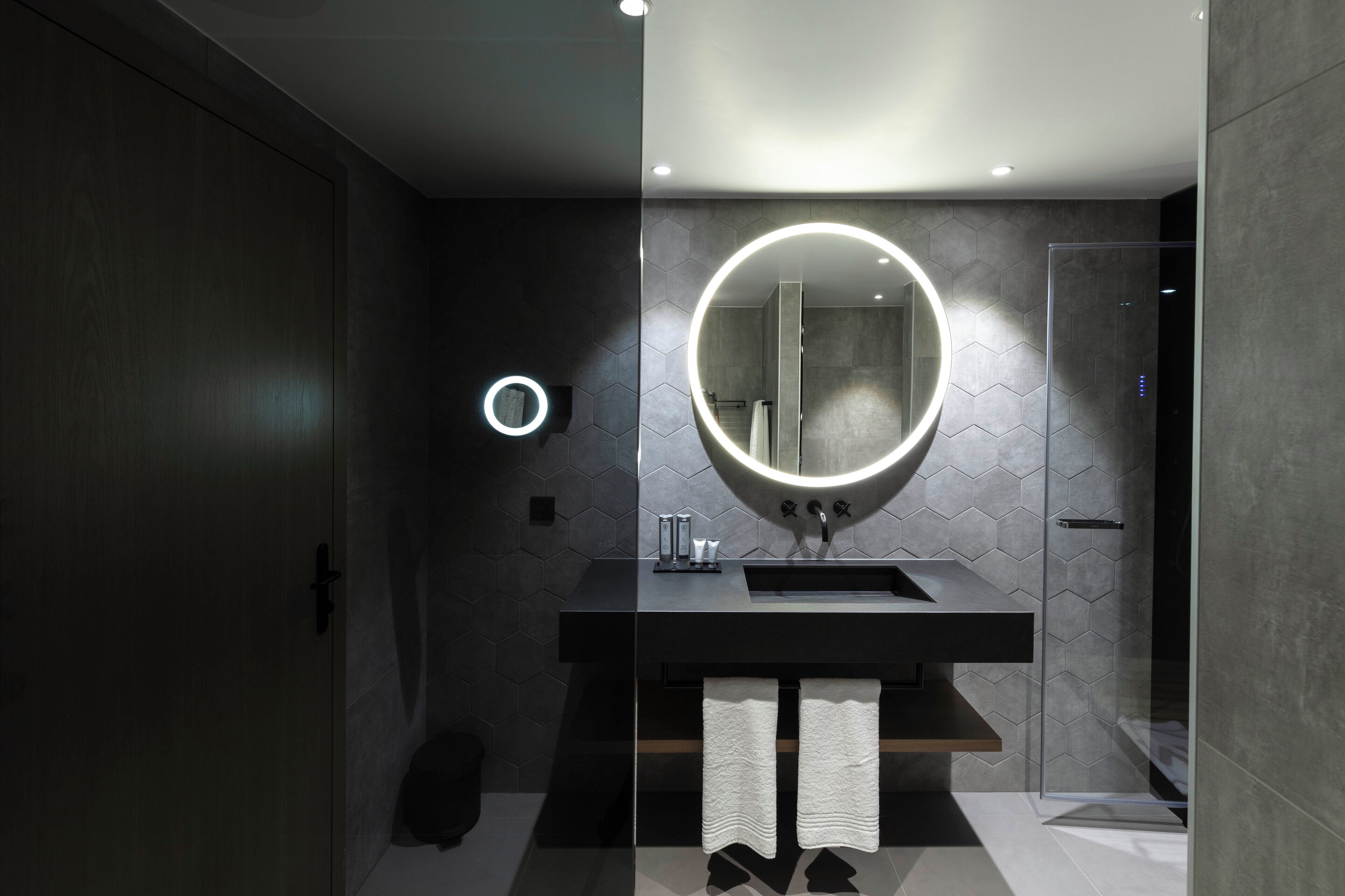 Een moderne badkamer met een grote spiegel, een ronde lamp en een douchecabine van glas.
