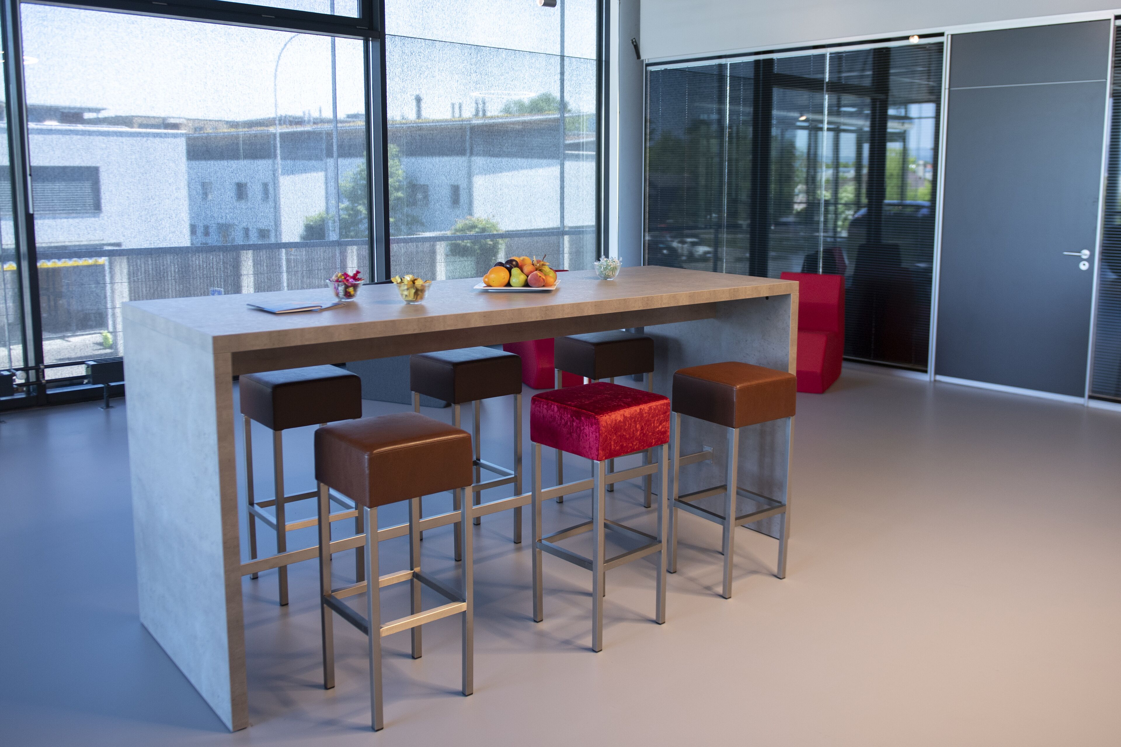 A modern bar area with a wooden table and four bar stools, one with a red cushion.