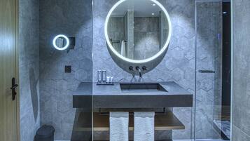 A modern bathroom with a glass-enclosed shower, a round mirror with integrated lighting, and a vanity with a sink and towel rack.