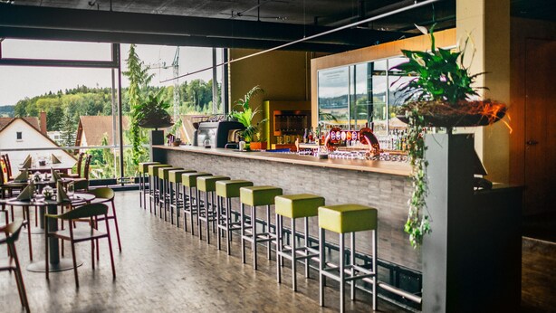 A bar area with a long counter, multiple stools, and a view of the outdoors. - Hotel Meilenstein (Langenthal)