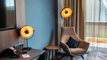 Habitación de hotel con cama, escritorio con teléfono, dos sillones, lámpara y televisor.
