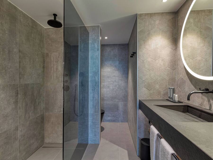 Un baño moderno con ducha envuelta en vidrio, un espejo grande y una encimera oscura.