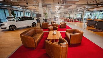 A modern showroom with a white car, leather chairs, a wooden table, and a red carpet.