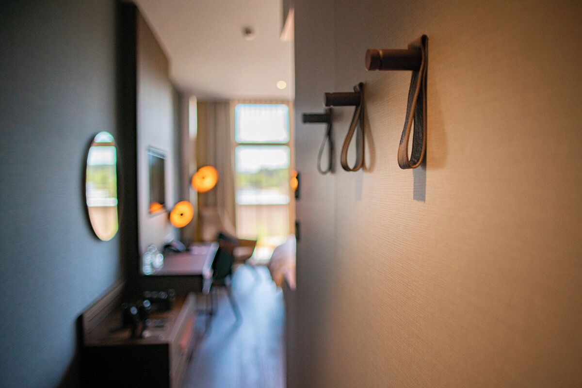 A hallway with a mirror, a towel rack, and a window with a view of a room.