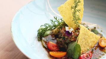 A plate of food with a blue bowl, including a tortilla chip, tomato, and greens.