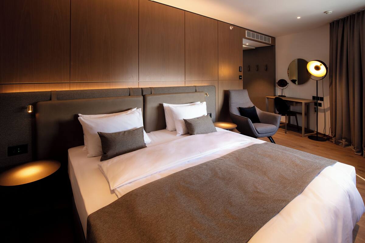Una habitación de hotel moderna con una cama grande, dos mesitas de noche, un escritorio y una silla.