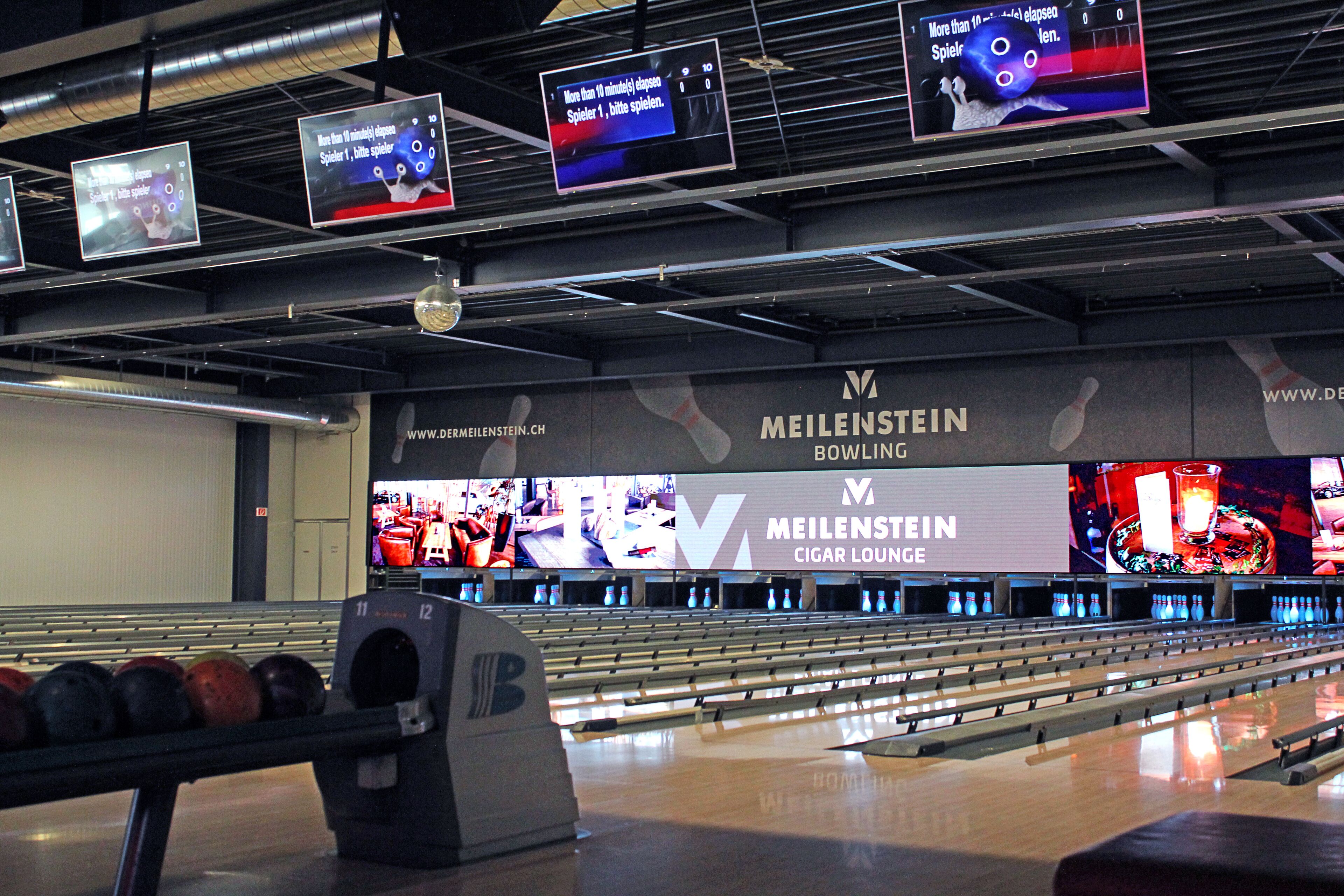Bolera con múltiples carriles, una pizarra de puntuación y un gran anuncio de Meilenstein Bowling.
