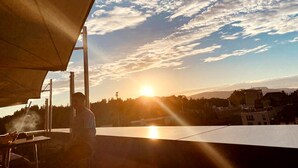 A person grilling outdoors with a clear view of the sunset and a cityscape in the background. - Hotel Meilenstein (Langenthal)