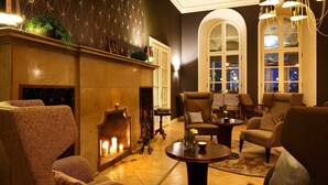 Un salon confortable avec des fauteuils moelleux, une cheminée et une vue sur la ville la nuit.