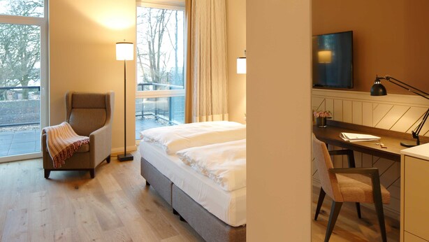 Une chambre d’hôtel équipée d’un lit, d’un bureau, d’une chaise, d’une télévision et d’une fenêtre donnant sur des arbres.
