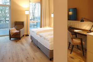 Une chambre d’hôtel équipée d’un lit, d’un bureau, d’une chaise, d’une télévision et d’une fenêtre donnant sur des arbres.