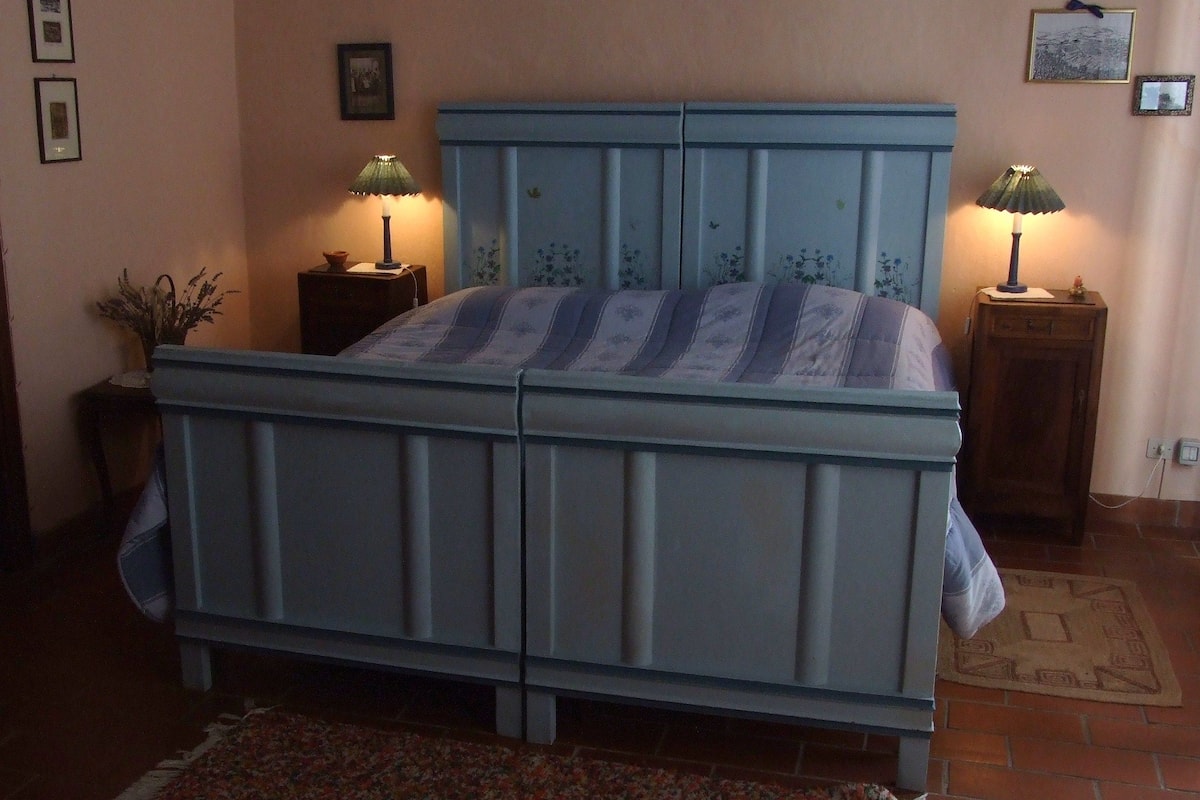 A bedroom with a double bed, two bedside tables with lamps, a floral rug, and a brick wall.