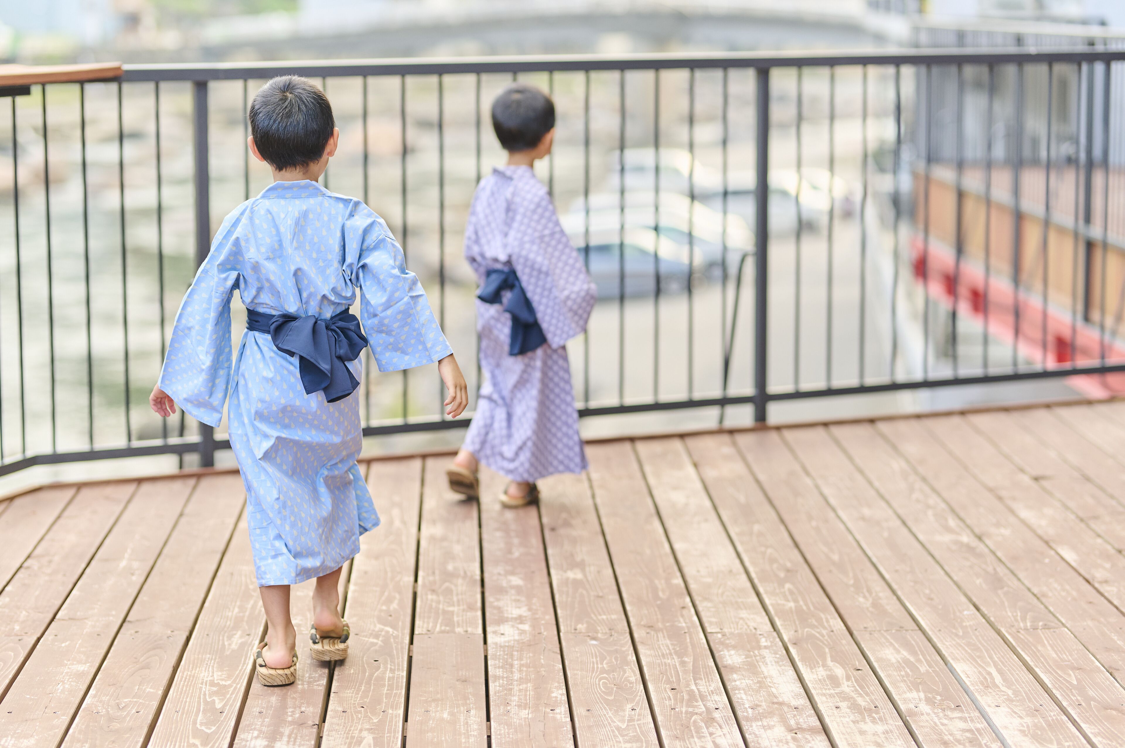 Two children in traditional attire walking on a wooden deck with a metal railing.