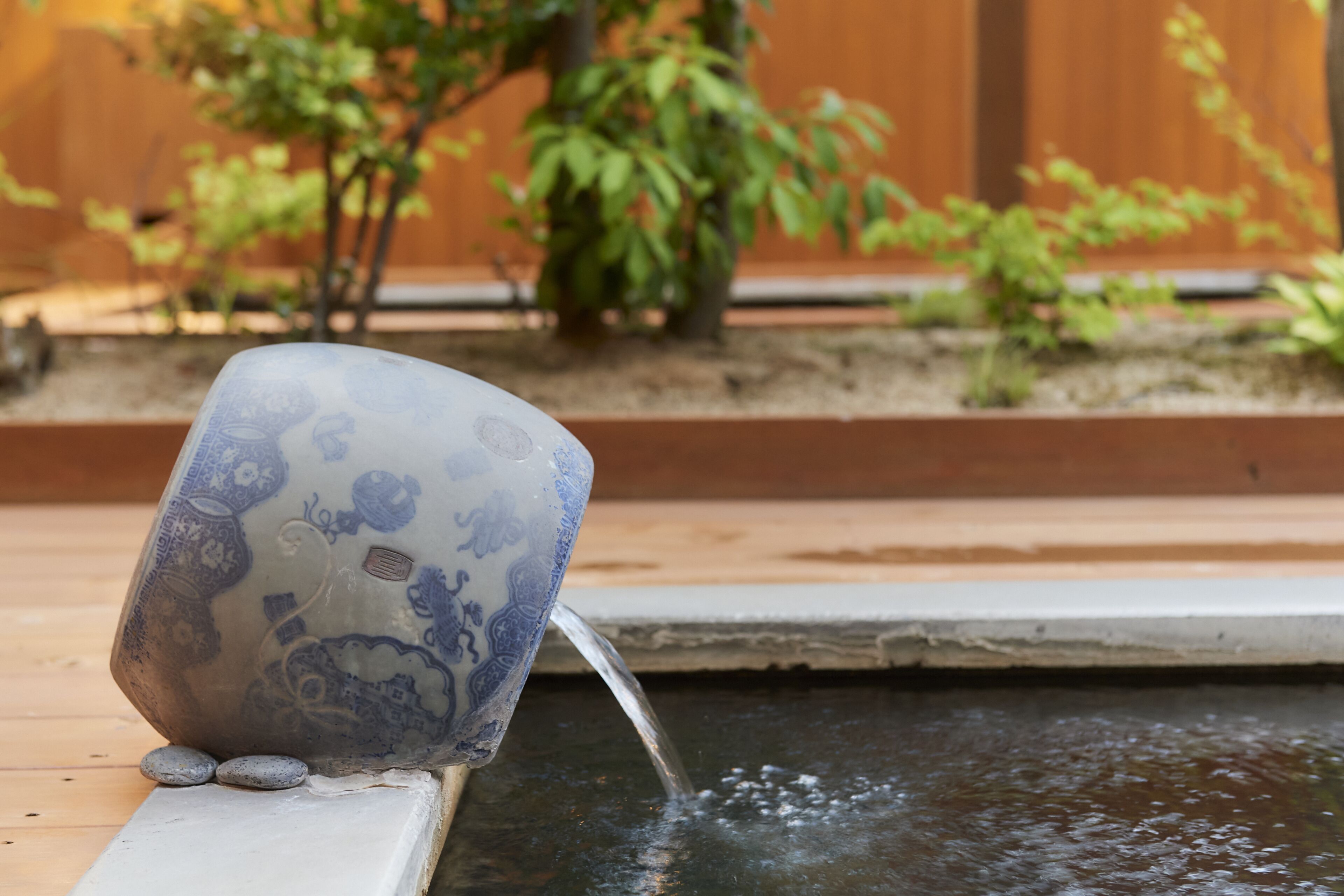 A decorative ceramic cup with intricate designs, placed on a ledge beside a small water feature.