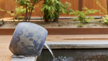 A decorative ceramic cup with intricate designs, placed on a ledge beside a small water feature.