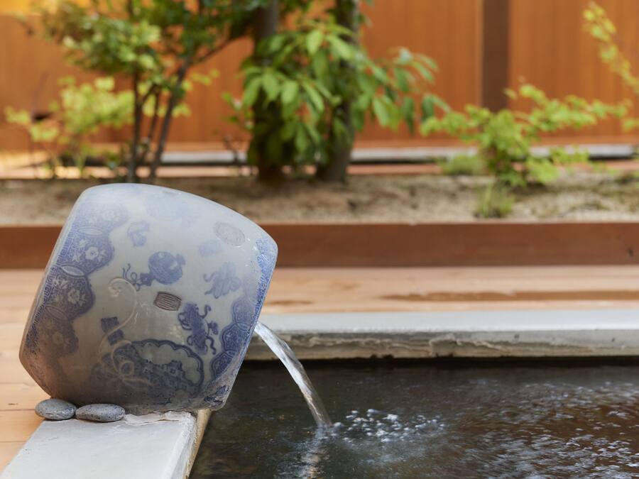 A decorative ceramic cup with intricate designs, placed on a ledge beside a small water feature.