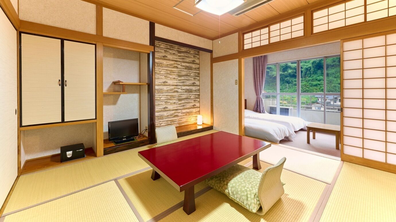 A traditional Japanese room with tatami flooring, a low table, a television, and a bed with a view of greenery.