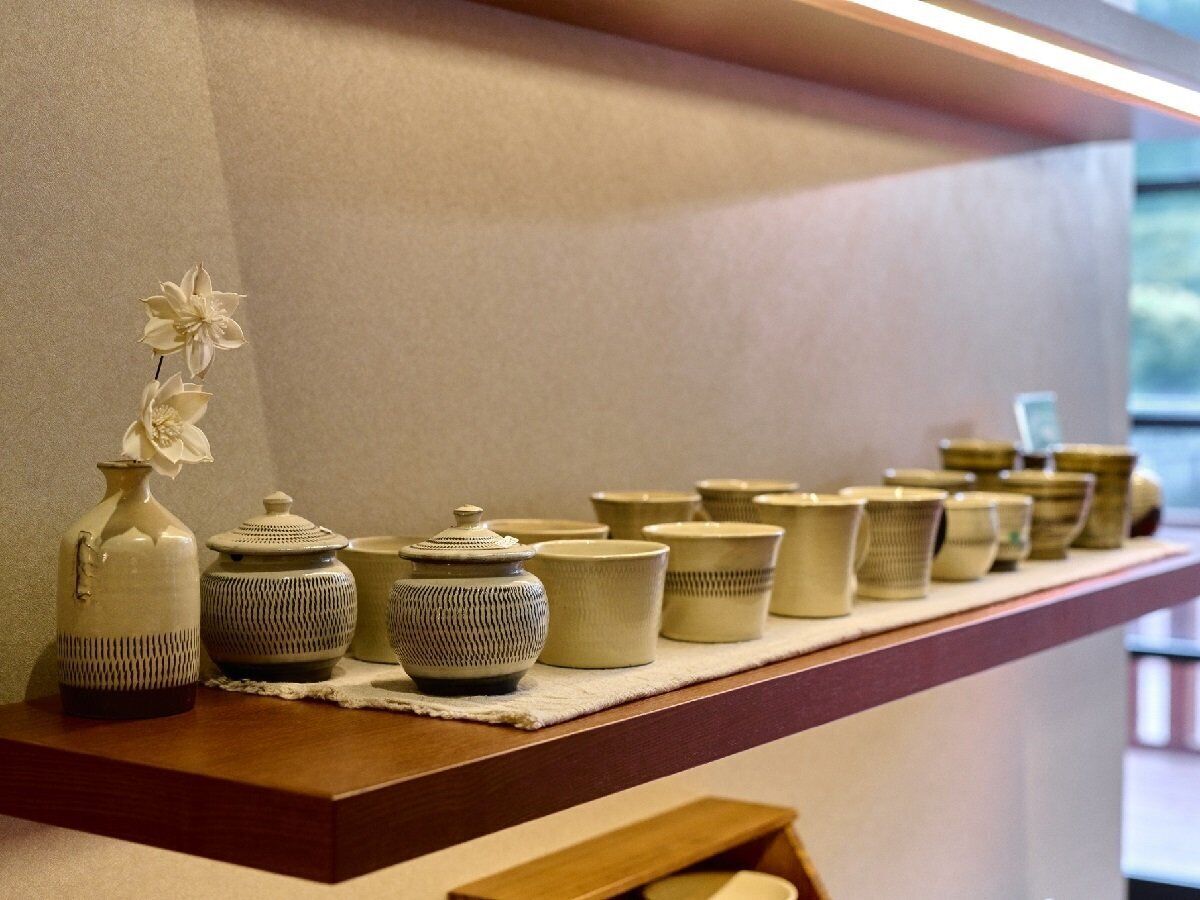 Uma prateleira com vários recipientes de cerâmica e um vaso com flores.