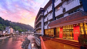 A hotel with a riverside view, featuring a multi-story building with balconies and a red facade. - Amagase Onsen Seitenkaku (Hita)