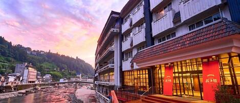 A hotel with a riverside view, featuring a multi-story building with balconies and a red facade.