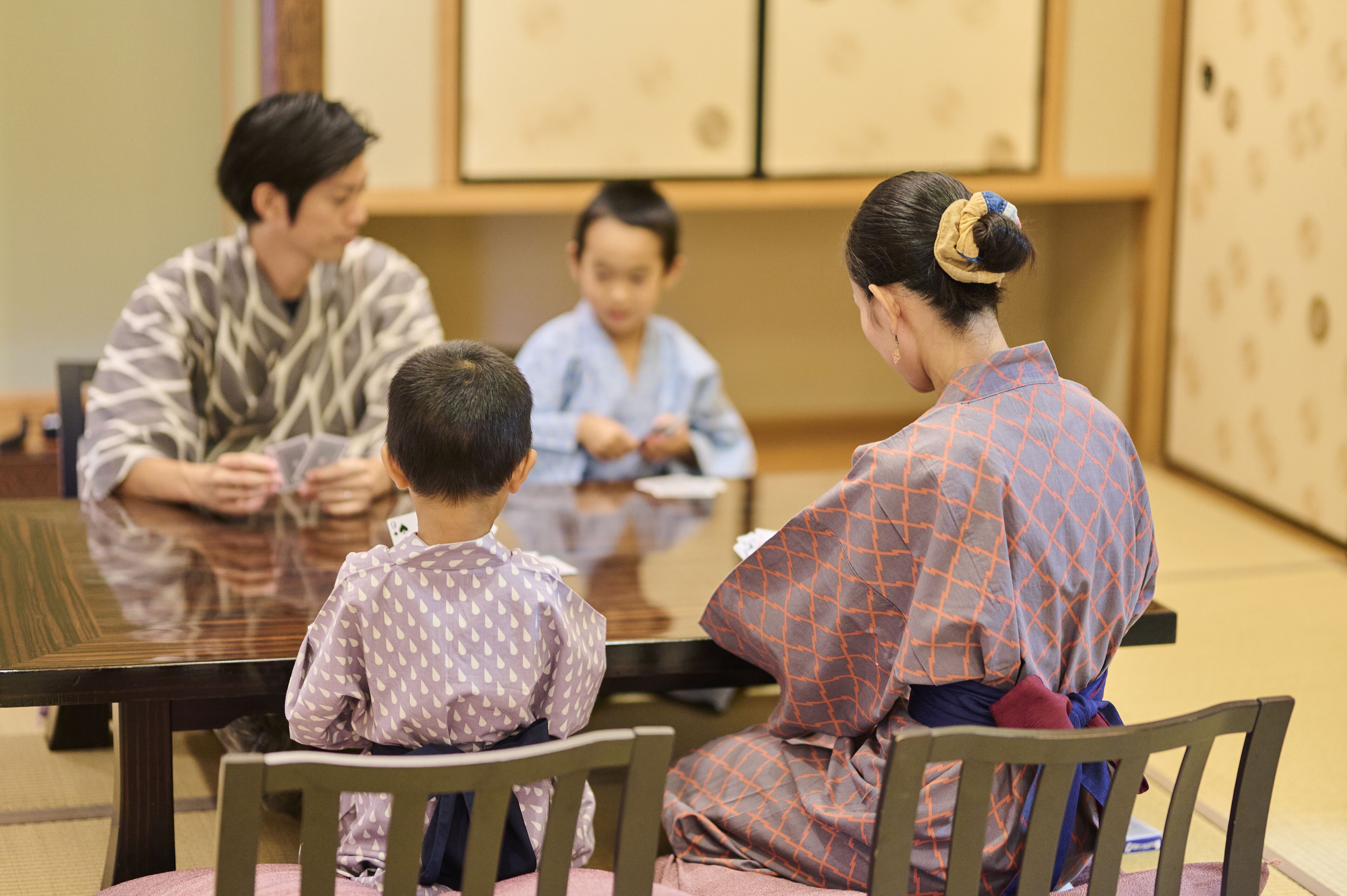 A family of four seated at a wooden table in a traditional setting with tatami flooring.
