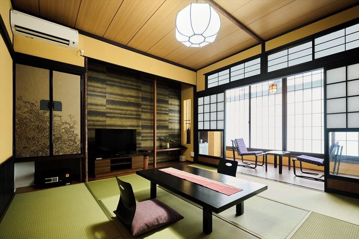 Ein traditioneller japanischer Raum mit Tatami-Böden, einem niedrigen Tisch mit rosa Unterlage und einem Fernseher auf einem Holzständer.