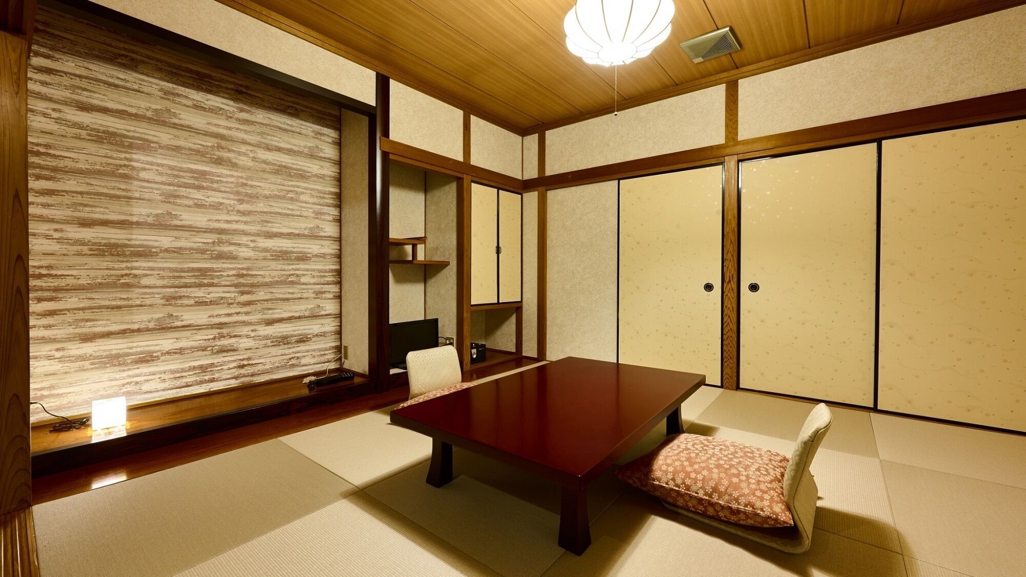 A traditional Japanese room with tatami flooring, a low wooden table, a cushioned bench, sliding doors, and a ceiling fan.