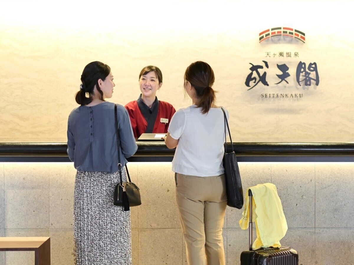 Three people at a reception desk with a sign above that reads "SEITENKAKU".