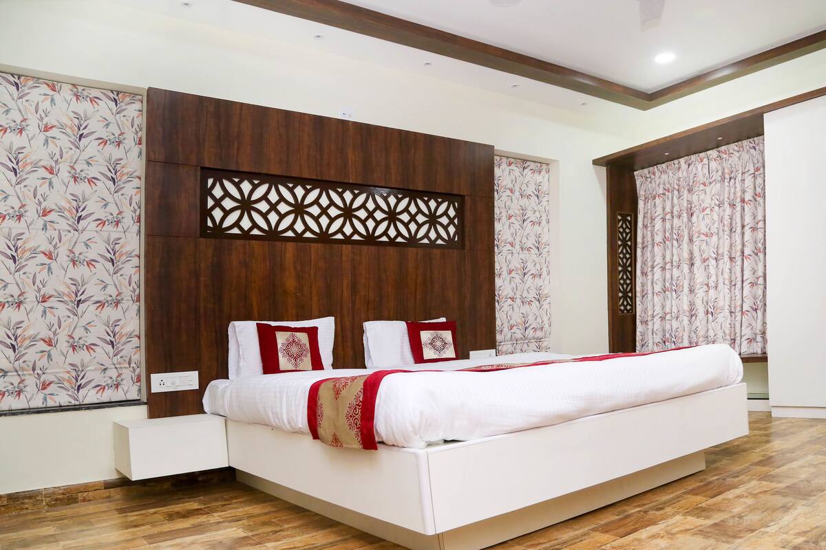 A modern bedroom with a wooden headboard, a white bed with red accents, and a patterned wall.
